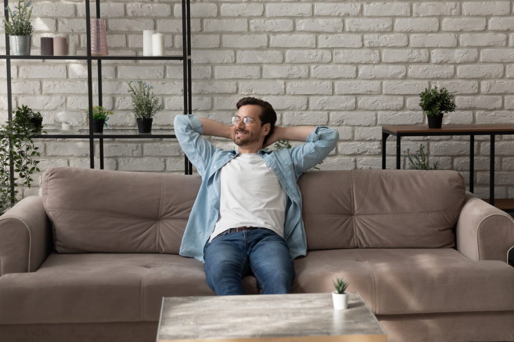 Calm millennial man relaxing on comfy sofa after finishing work
