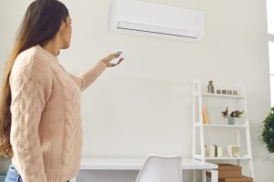 Young woman standing in living-room and switching on air conditioner with remote control