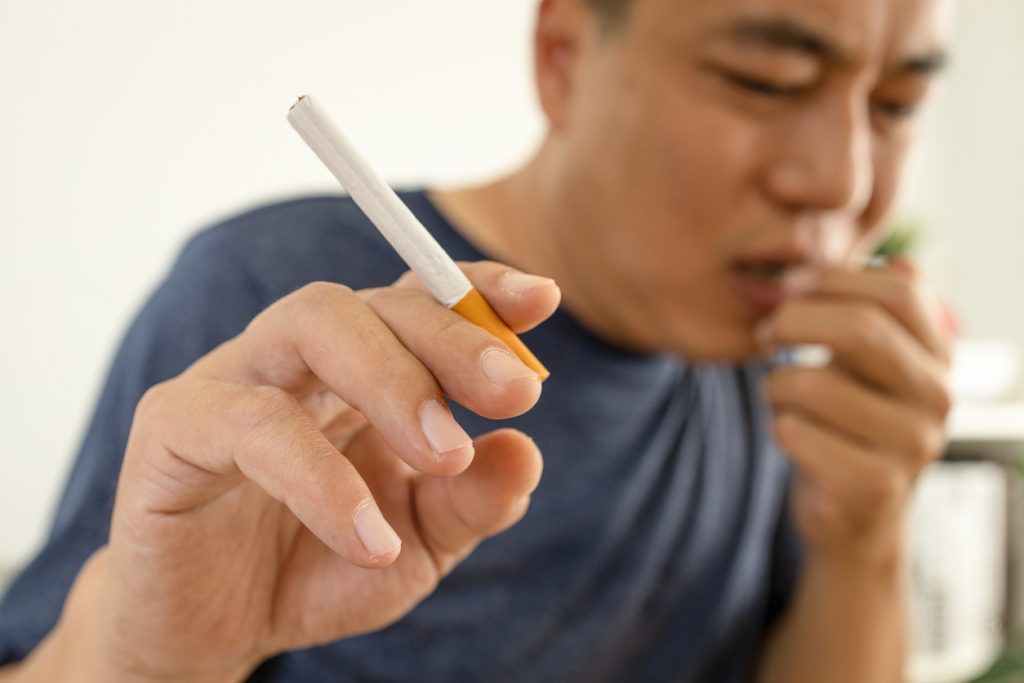 Male smoker holding a cigarette suffering from chronic cough,asian man patient coughing with sputum,respiratory problems,emphysema disease or lung cancer from smoking,medical and health care concept