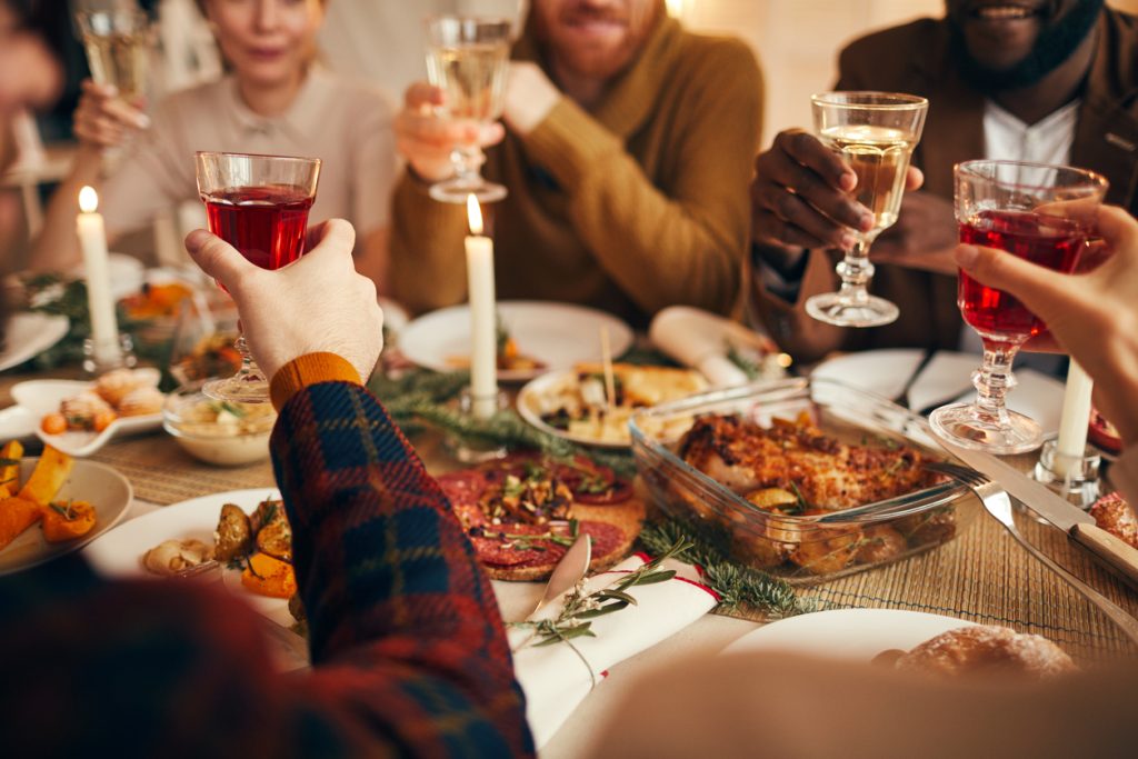 Close up of modern adult people raising glasses while enjoying Christmas dinner at home