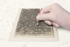 person gloved check ventilation in the dirt with a cotton swab, cleaning dusty ventilation grilles, on a moldy white wall